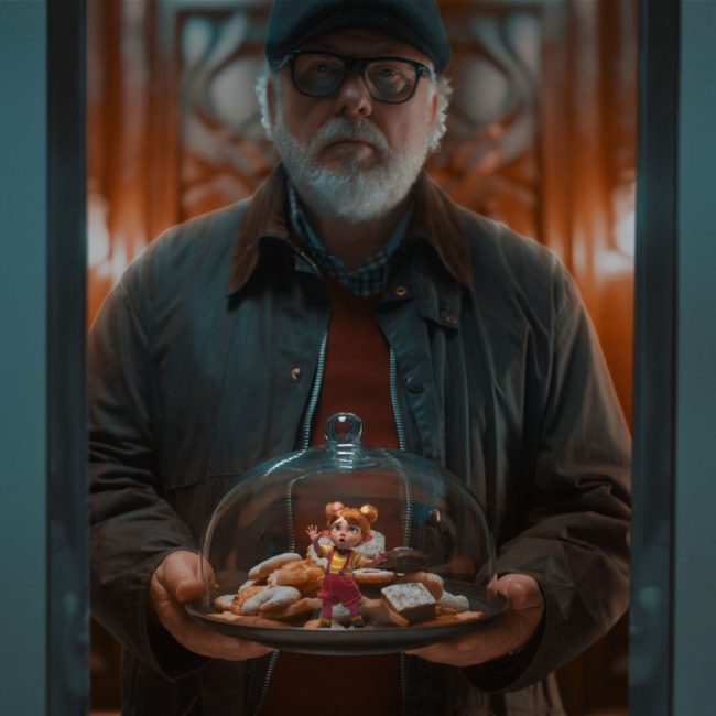An elderly man holds a glass-covered tray of pastries with a tiny red-haired CG fairy standing inside.