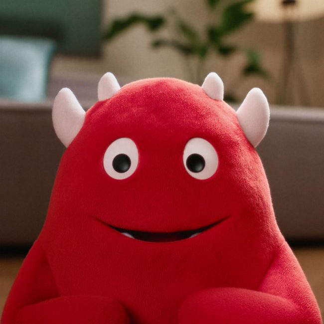 Close-up of the red Woom Buddy 3D character sitting in a family living room.